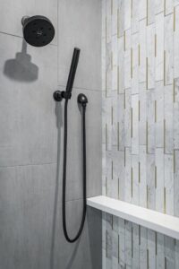 A modern black shower head and handheld sprayer installed in a tiled shower by Thimijan Custom Homes LLC in Rochester, MN