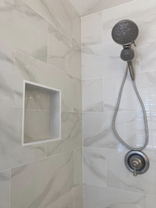 Close-up of modern shower fixtures and a tiled storage niche in a bathroom remodel by J.C.Improvement in Katy, TX.