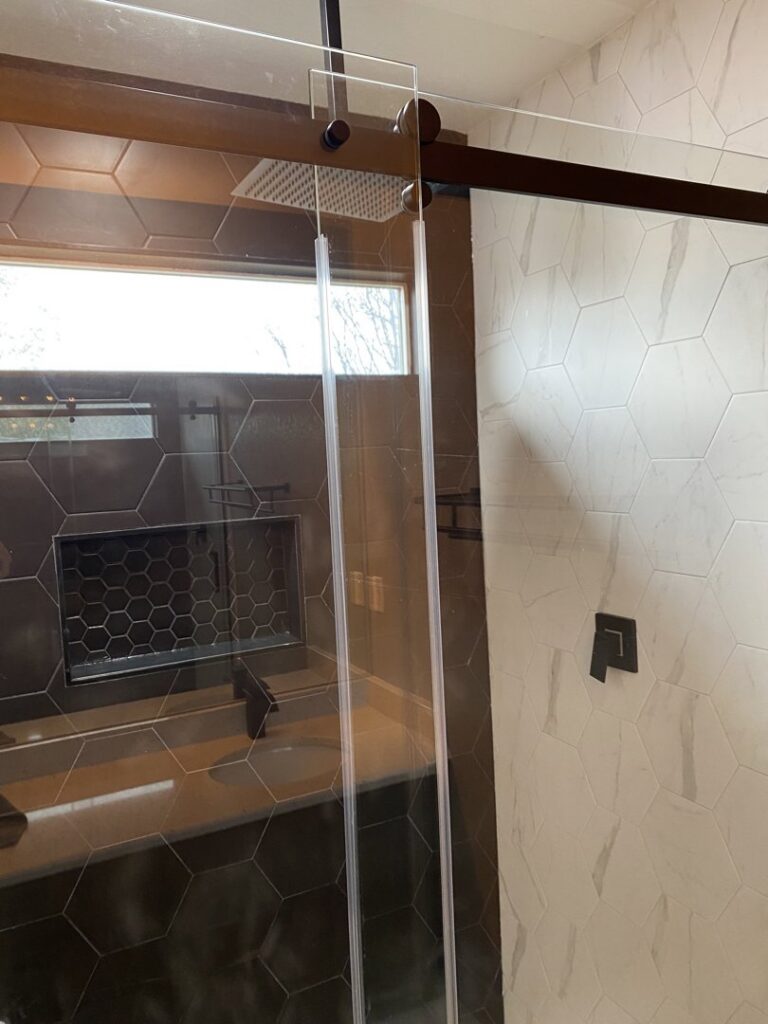 A modern shower with clear glass doors and hexagonal wall tiles, a renovation by Handyman Connection of Fort Collins in Fort Collins, CO