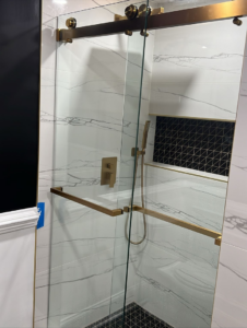 A modern shower with elegant glass doors, gold-toned fixtures, and marble-patterned tiles installed by Home Renovation & Design in Trumbull, CT.