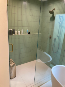 A modern shower with green subway tiles, a glass door, and a built-in shelf completed by Tess Tile By Design in Kansas City, MO.