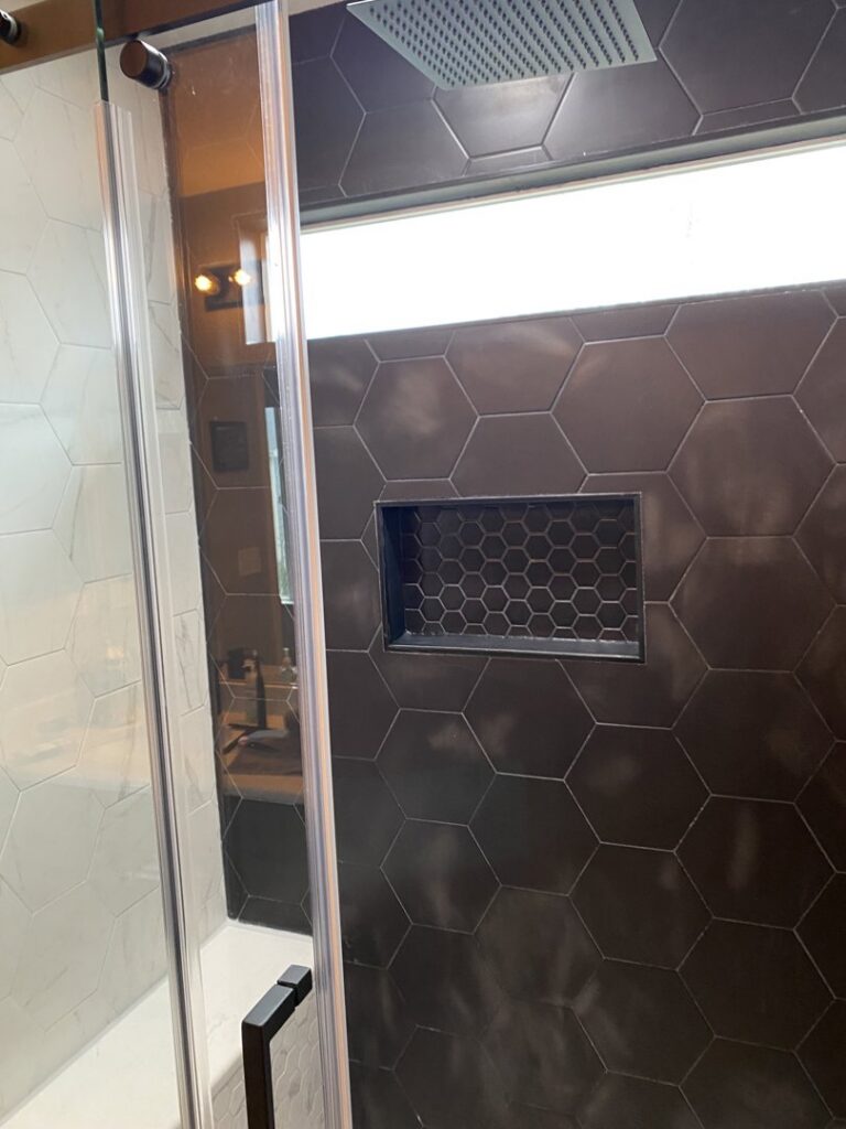 A modern shower with dark hexagonal tile and a built-in niche, completed by Handyman Connection of Fort Collins in Fort Collins, CO