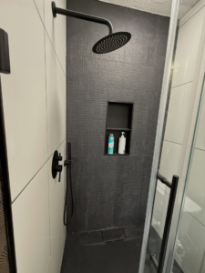 A modern shower with black textured tiles and a rain shower head installed by Waking Up Construction in Oklahoma City, OK
