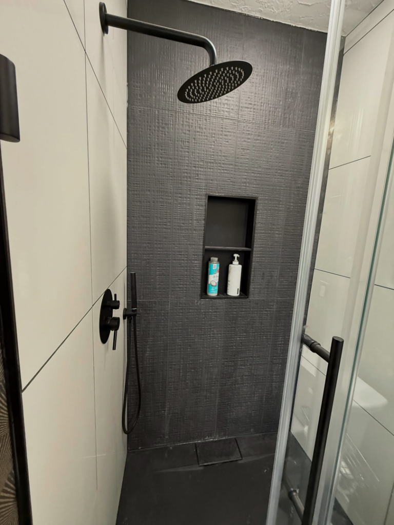 A modern shower with black textured tiles and a rain shower head installed by Waking Up Construction in Oklahoma City, OK