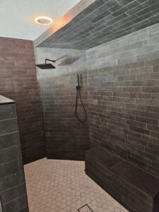 A modern shower remodel featuring dark subway tiles and a hexagonal floor by LJ Builders in Chandler, AZ