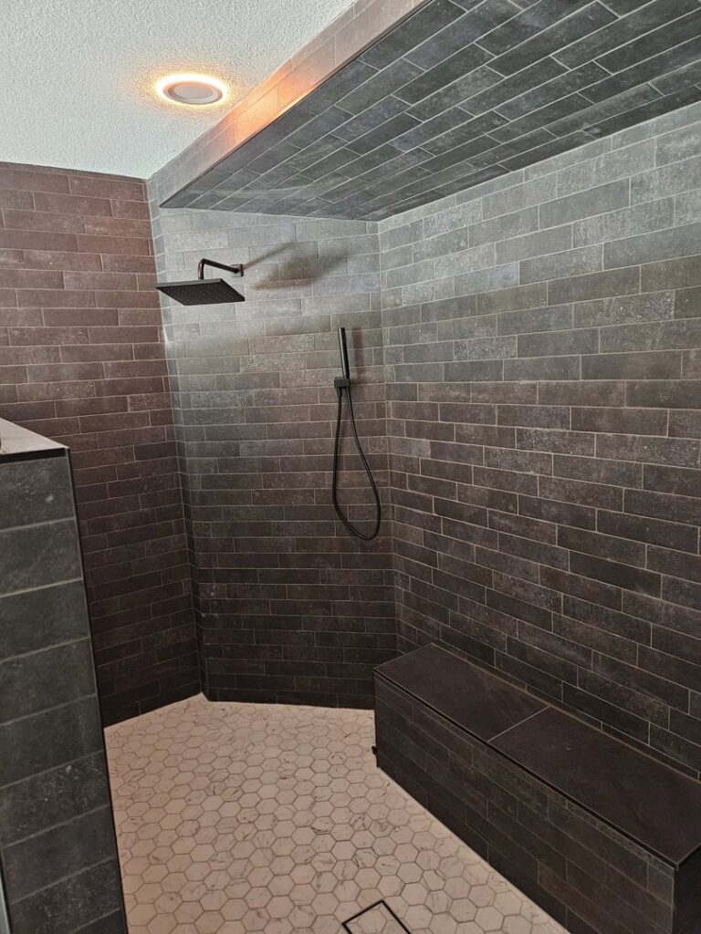 A modern shower remodel featuring dark subway tiles and a hexagonal floor by LJ Builders in Chandler, AZ