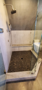 A modern shower renovation with pebble flooring and glass enclosure by JMS Construction in Las Vegas, NV