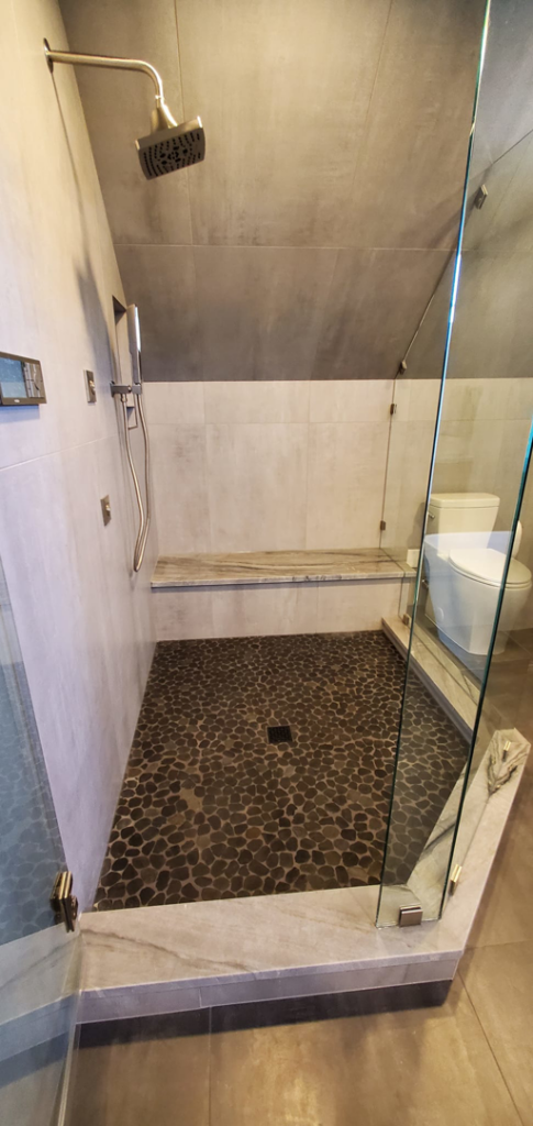 A modern shower renovation with pebble flooring and glass enclosure by JMS Construction in Las Vegas, NV