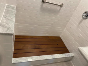 Modern shower renovation with white subway tiles, marble bench, and custom wooden floor by MTI Carpentry in Jersey City, NJ.