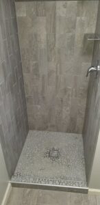 A modern shower stall with new grey wall and pebble floor tiles, installed by Excalibur Home Services in Council Bluffs, IA.