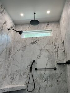 A modern shower with large marble-look tiles and black fixtures installed by Four Seasons Building & Remodeling in Mauldin, SC.