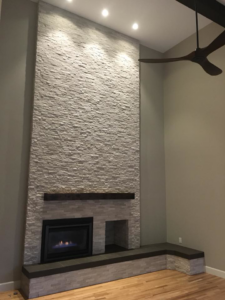 A modern stacked stone fireplace installation with a wooden mantel and gas insert by Bailey Contracting, LLC in Lake Oswego, OR.