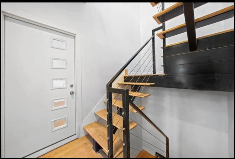 A modern staircase with wood treads and metal railings next to a new entry door by Revival Home Remodeling in Chicago, IL.