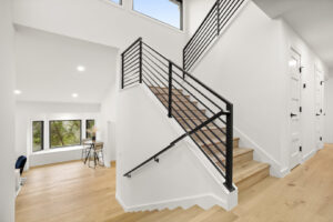 A contemporary staircase featuring black metal railings and light wood steps, part of a renovation by Proper 3 Renovations in Austin, TX