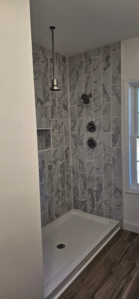 A modern walk-in shower with marble-look tile and multiple showerheads, completed by Susquehanna Valley Builders in Harrisburg, PA.