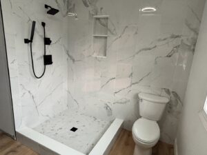 A modern tiled shower with white marble-look tiles, black shower fixtures, and a new toilet, completed by Blas Home Remodeling LLC in New Castle, DE.