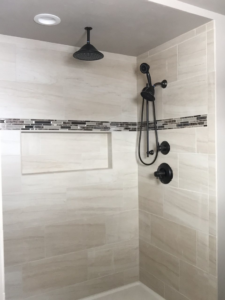 A modern tiled shower with new black fixtures and a mosaic accent installed by Fueled Up Flooring- Justin Watruba in Eau Claire, WI.