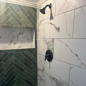 A modern tiled shower with dark bronze fixtures and green herringbone tiles by City Home Improvement Inc in Portland, OR.