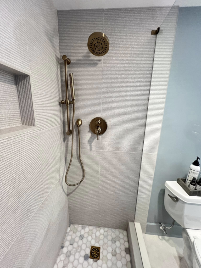 A modern tiled shower installation featuring textured gray wall tiles and a pebble floor by Extra Mile Tile in Cincinnati, OH.