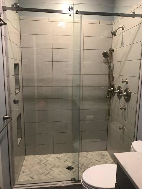 A modern tiled shower with a glass enclosure and herringbone floor pattern completed by FEARS Construction in Nashville, TN.