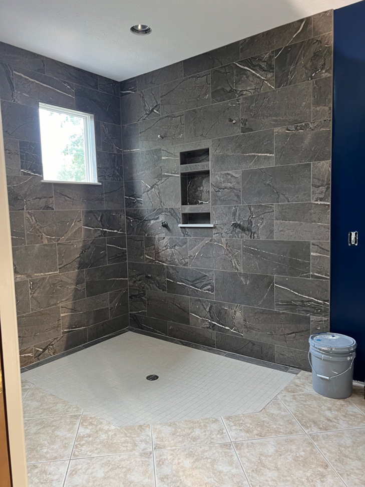 A modern tiled shower remodel with dark grey marble-look tiles by Lafayette Concrete & Remodel, LLC in Lafayette, IN