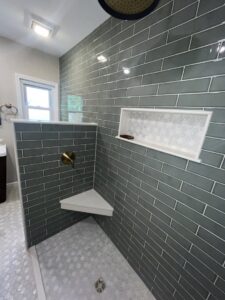A modern walk-in shower with green subway tiles and a built-in shelf installed by Stanley Contracting in Whiting, NJ