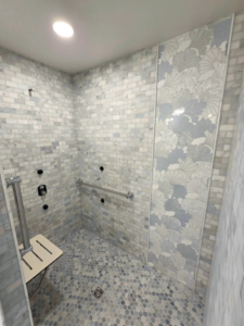 A modern tiled shower with a decorative leaf-patterned strip and safety features by Tyler the Tiler in Jefferson, WI.