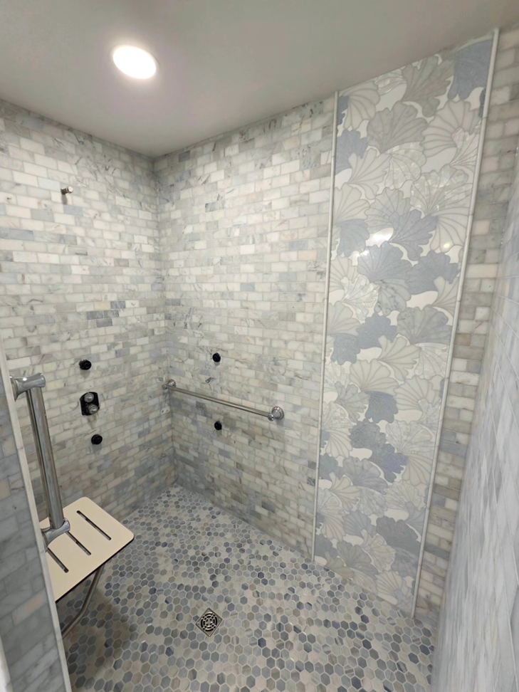 A modern tiled shower with a decorative leaf-patterned strip and safety features by Tyler the Tiler in Jefferson, WI.