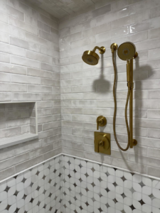 A modern tiled shower with gold fixtures and two tile patterns installed by Le Roux Homes in Enid, OK.