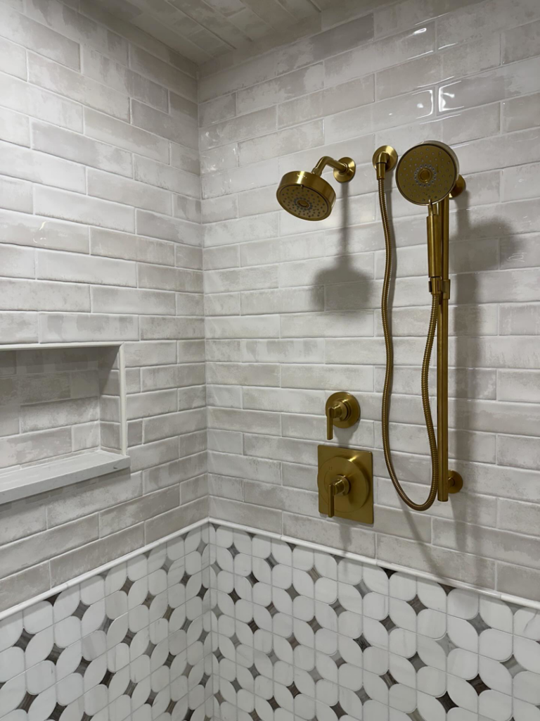 A modern tiled shower with gold fixtures and two tile patterns installed by Le Roux Homes in Enid, OK.