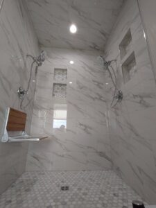 A modern walk-in shower with white marble-look tiles, two shower heads, and a built-in bench, installed by Devco Construction LLC in West Valley City, UT.