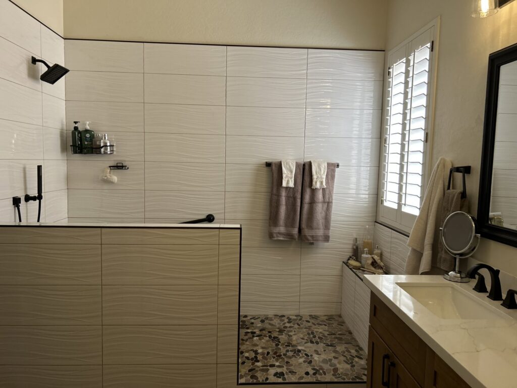 A modern walk-in shower bathroom renovation with textured white tiles and pebble flooring by AZ New Bath in Glendale, AZ