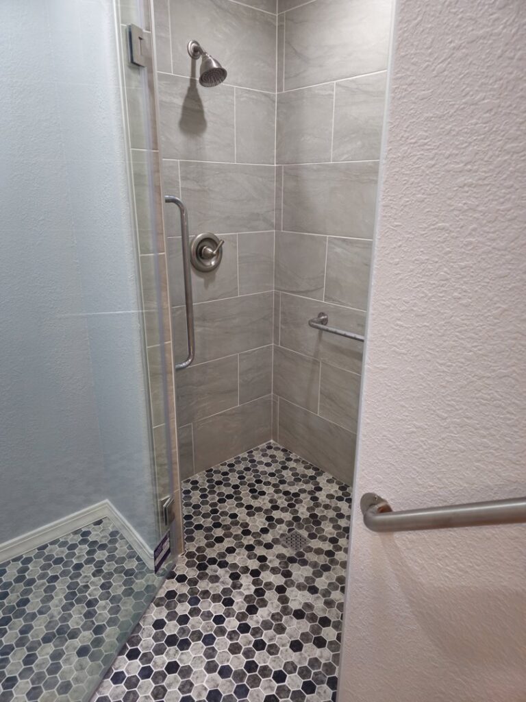 A modern walk-in shower featuring grey tiled walls and a hexagonal tiled floor, installed by Jedi Bldrs in Colorado Springs, CO.