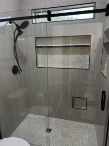 A modern walk-in shower with grey tiles and a glass sliding door, installed by Centennial Builders, LLC in Litchfield Park, AZ.