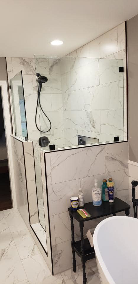 A modern walk-in shower with black fixtures and white tile installed by Heritage Design & Remodel in Raleigh, NC.