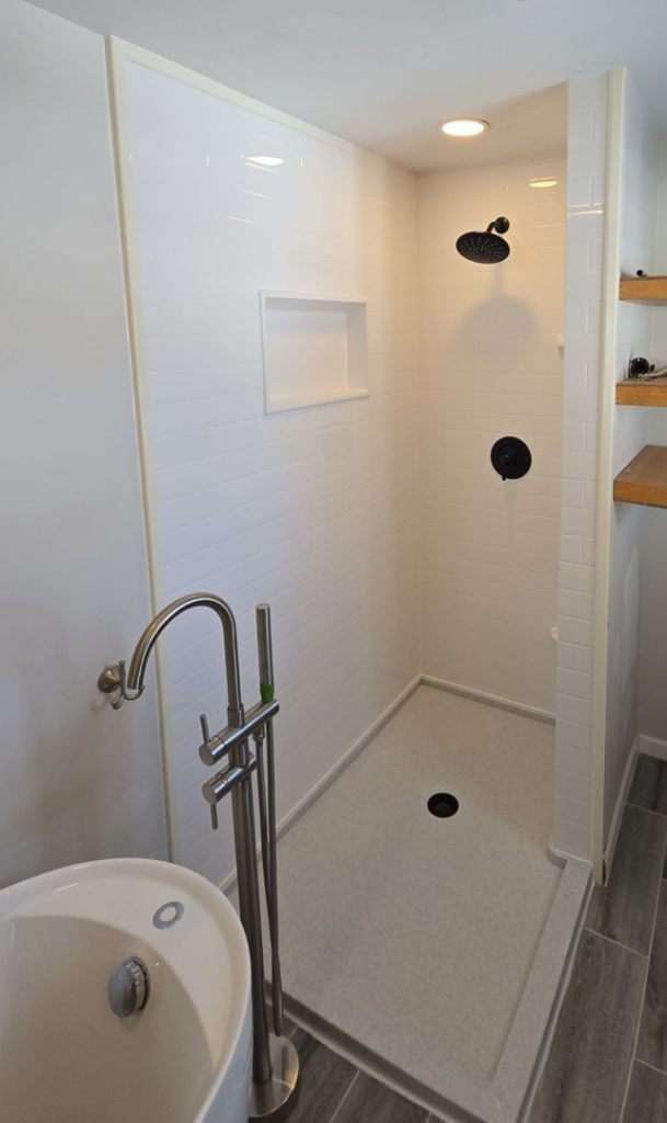 A modern walk-in shower installation with white tiled walls and dark fixtures by The Shower Company in Kansas City, MO.