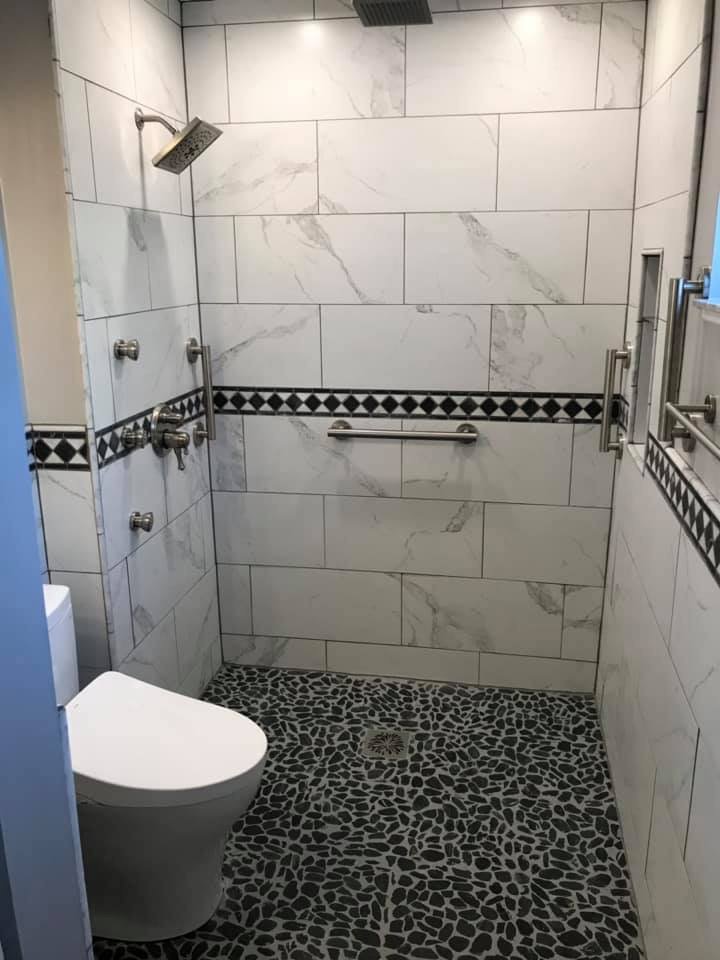 A modern walk-in shower with white and black tile, grab bars, and a pebble floor installed by Pro Remodel LLC in St. Charles, MO.
