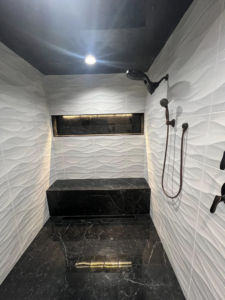 A modern walk-in shower with textured white wall tiles, black marble floor, built-in bench, and niche by Patriot Tile LLC in Skiatook, OK.
