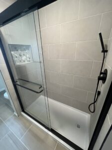 A modern walk-in shower with a glass door, grey large format tiles, and a built-in niche by MPH Design in Philadelphia, PA.
