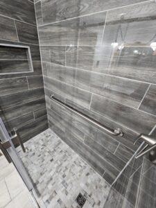 A modern walk-in shower featuring dark wood-look tiles and a mosaic floor, installed by Jedi Bldrs in Colorado Springs, CO.