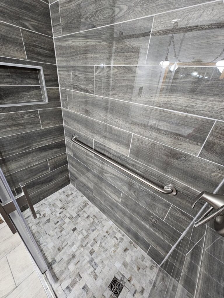 A modern walk-in shower featuring dark wood-look tiles and a mosaic floor, installed by Jedi Bldrs in Colorado Springs, CO.