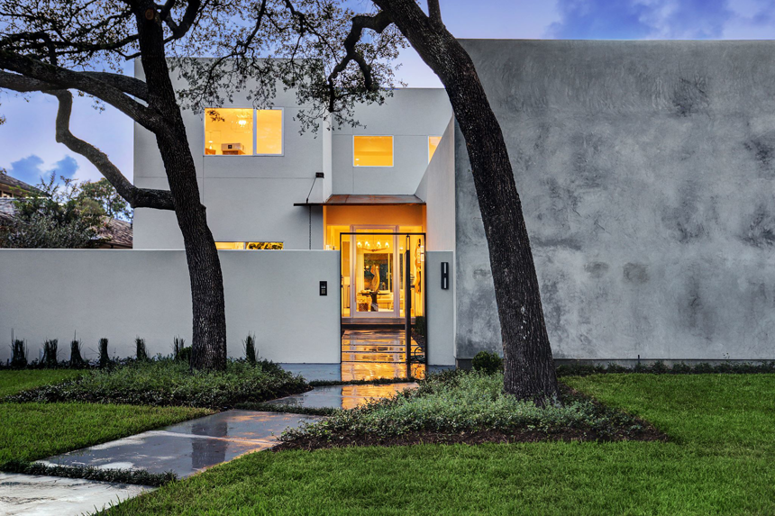 A modern white house exterior with a well-lit entrance at dusk, built by Allan Edwards Builder Inc in Houston, TX.