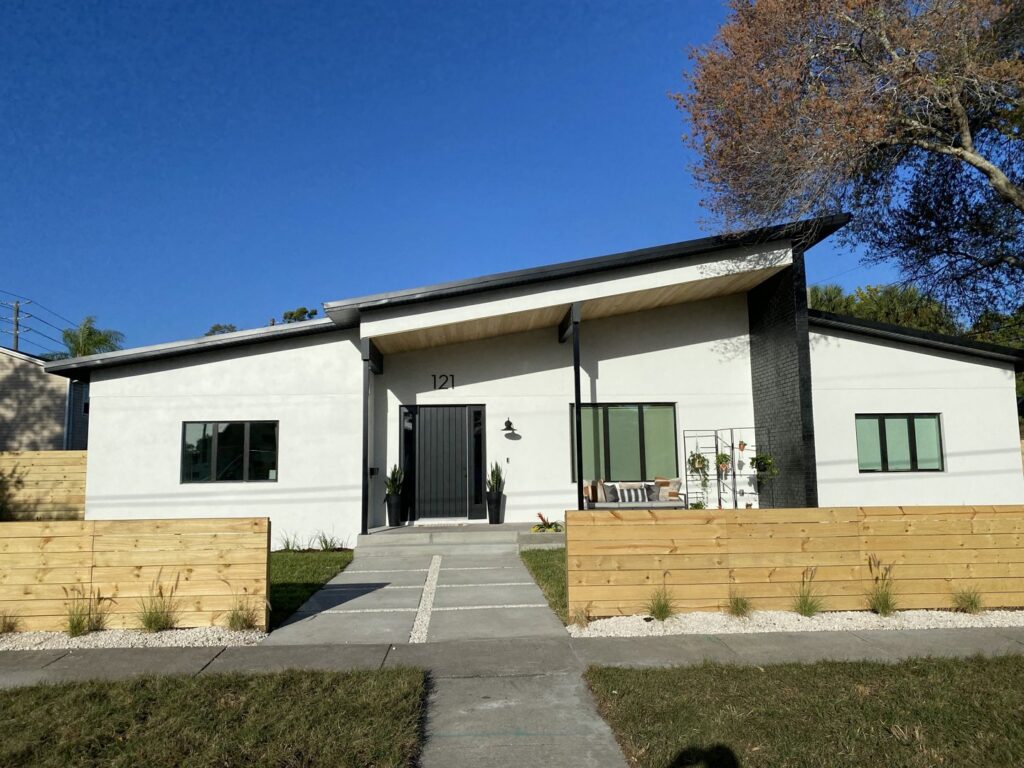 The exterior of a modern white house with a striking black roof and wooden fence, a completed project by Pioneer Built in St. Petersburg, FL.