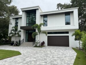 Contemporary white house exterior with dark garage door and paved driveway by Charter Bay Home Builders in Tampa, FL