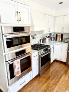 A modern white kitchen with gold hardware, built-in ovens, and a gas range by Cincinnati Cabinet Refacing in Cincinnati, OH.