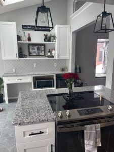 A modern white kitchen remodel with grey backsplash and a large island with a stovetop by Advanced Remodeling Services in Elbert, CO.