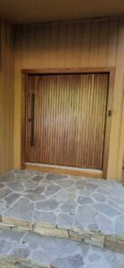A newly installed modern wooden front door with vertical slats and a long black handle by M J Services Home Remodeling in Gaithersburg, MD.