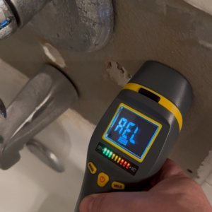 A handyman using a moisture meter to inspect for water damage near a faucet at Chris Pierce Construction in Sioux City, IA.