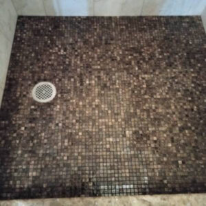 Close-up of a mosaic tiled shower floor with a central drain, installed by True Alchemy - Tile & Grout Restoration in Denver, CO.