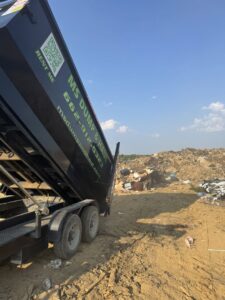 An MS Dump & Haul dumpster being unloaded at a landfill or large debris pile in Hernando, MS.
